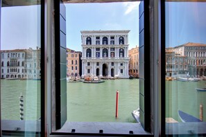 A view of a historic building with a large arched entrance, a canal with boats, and a red pole in the water. - GRITTI Grand Canal (Venice)