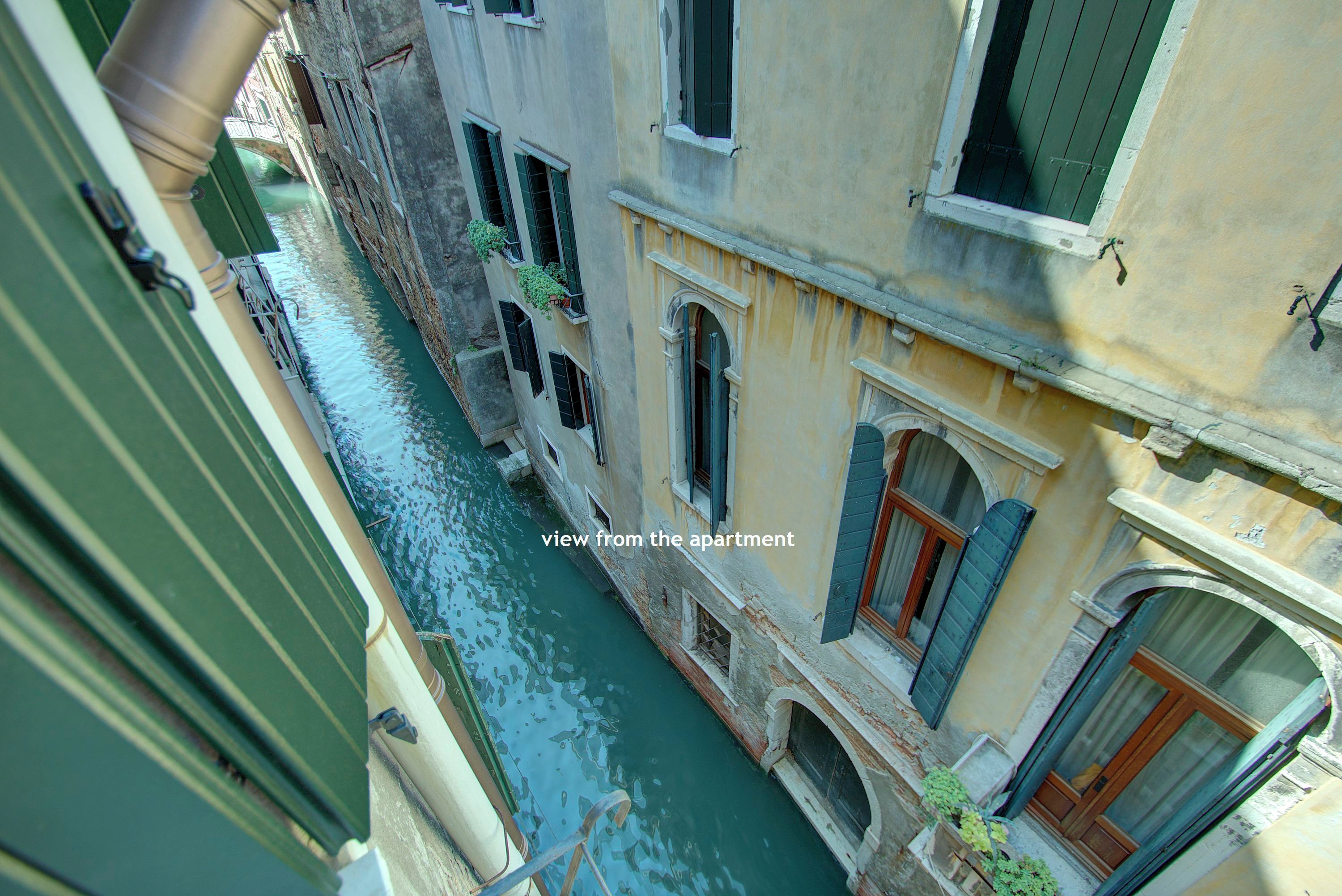 A narrow canal with buildings on either side, a view from an apartment overlooking the water.