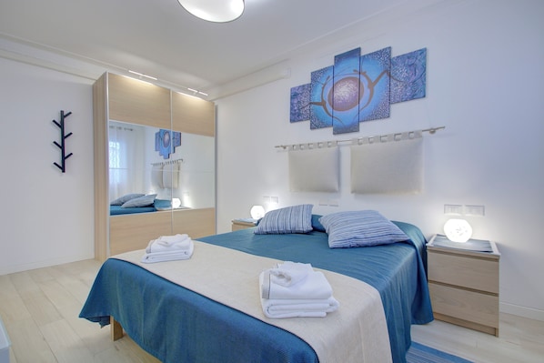 A modern bedroom with a large bed, bedside tables, a mirror, and artwork on the wall.