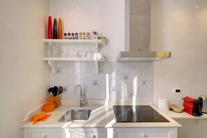 A modern kitchen with a stainless steel sink, a built-in oven, and a range hood. There are shelves above the sink holding various kitchen items. - BAROCCO-Veneziano (Venice)