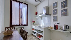 A kitchen with a wooden table, white cabinets, a window with curtains, and a wall with framed pictures.