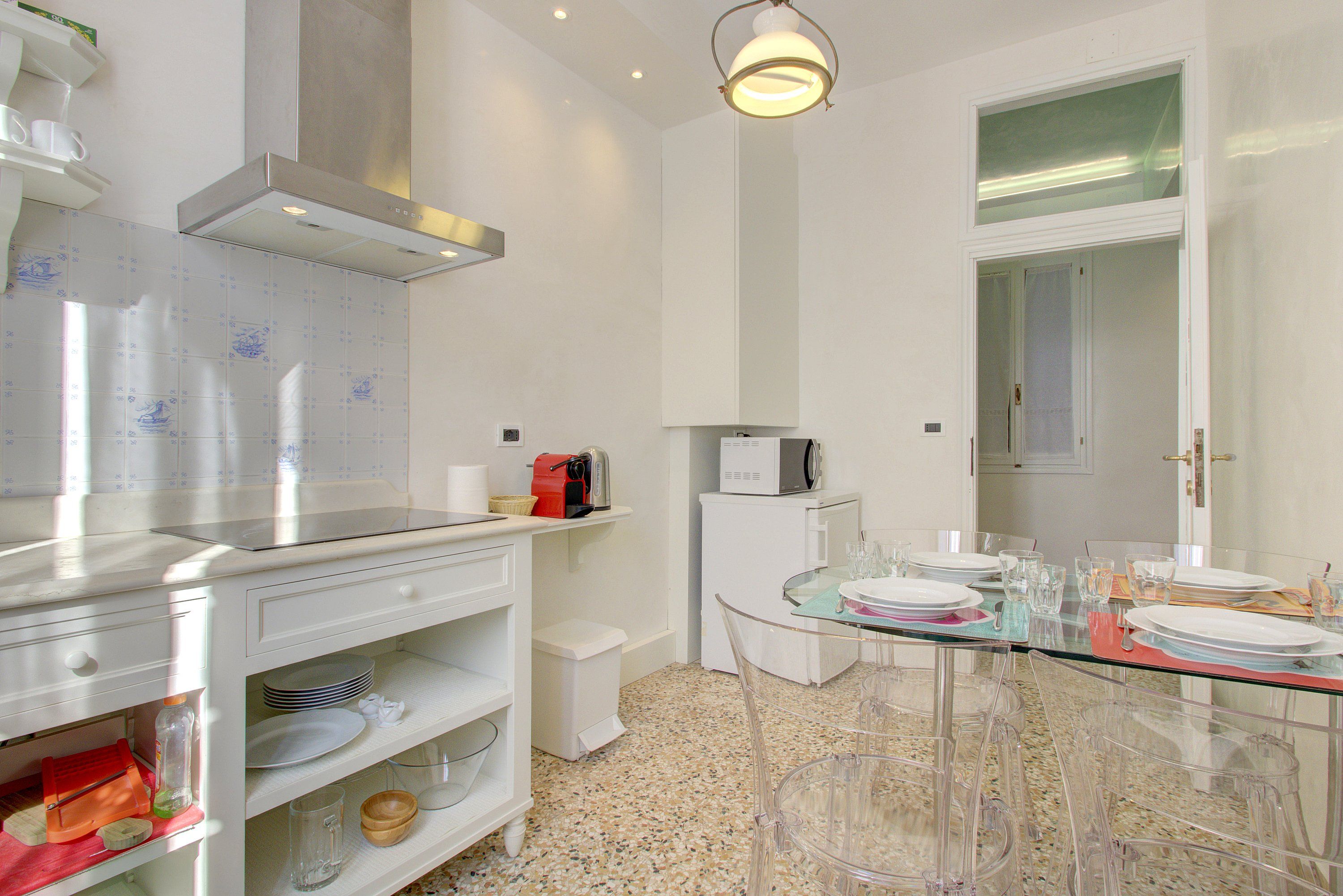 A modern kitchen with white cabinetry, a stainless steel range hood, a microwave, and a glass dining table with chairs.