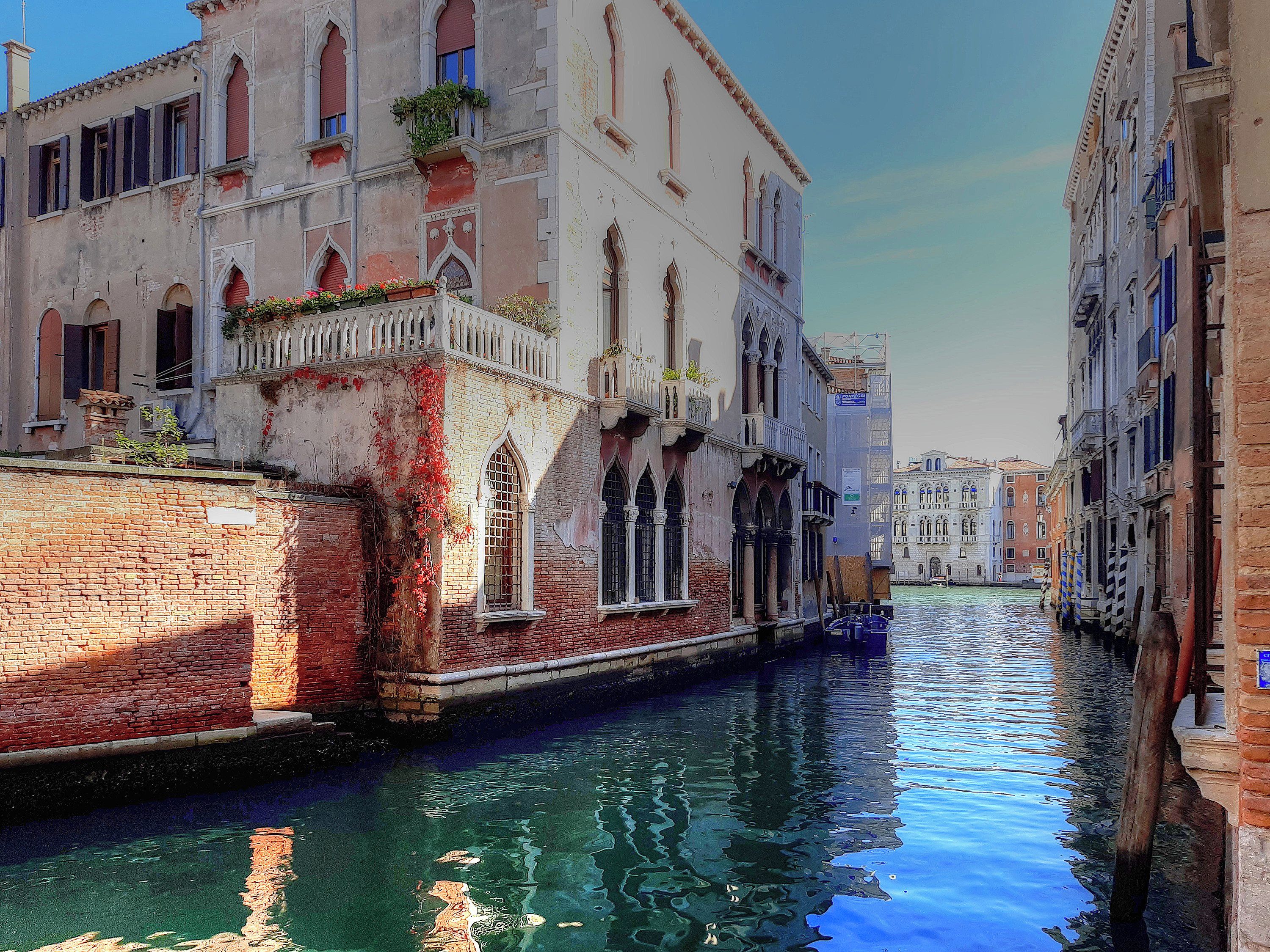 A narrow canal with buildings on either side, featuring arched windows and balconies.