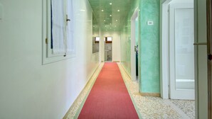A hallway with a red carpet, white walls, and a green accent wall. There are doors on both sides and a window at the end.