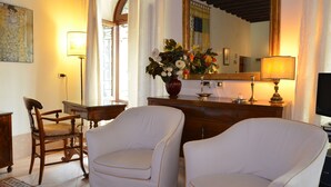 Una habitación con dos sillones blancos, un escritorio de madera, un florero, un espejo y una lámpara.