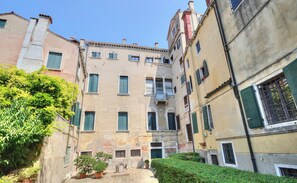 Una calle estrecha flanqueada por edificios, con balcones y un pequeño jardín.