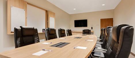 A conference room with a long table, black leather chairs, whiteboards, and a TV on the wall.