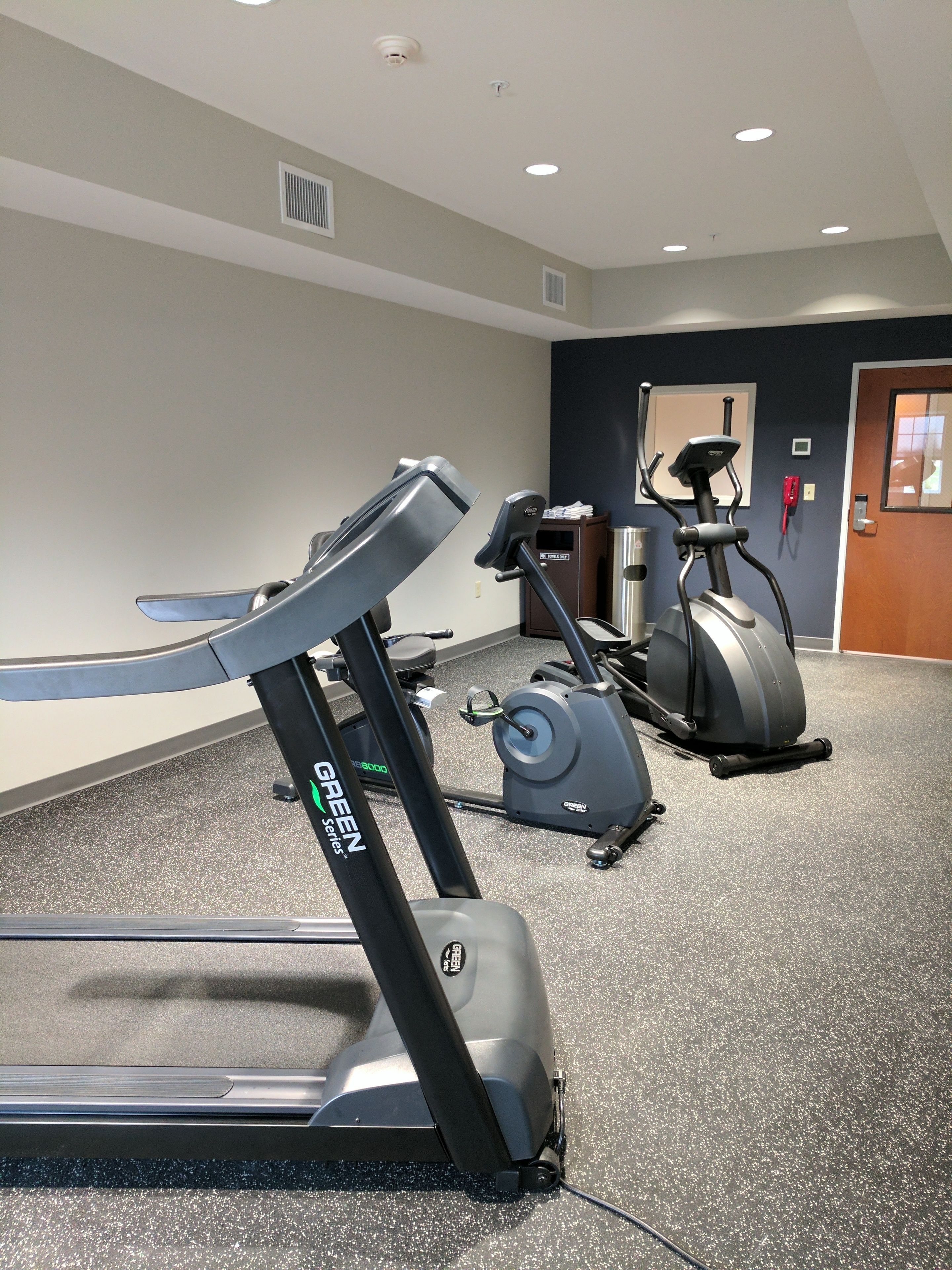 A gym with a treadmill, an elliptical, and a stationary bike, with a door and a small window in the background.