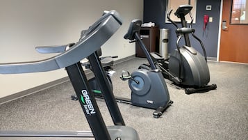 A gym with a treadmill, an elliptical, and a stationary bike, with a door and a small window in the background.