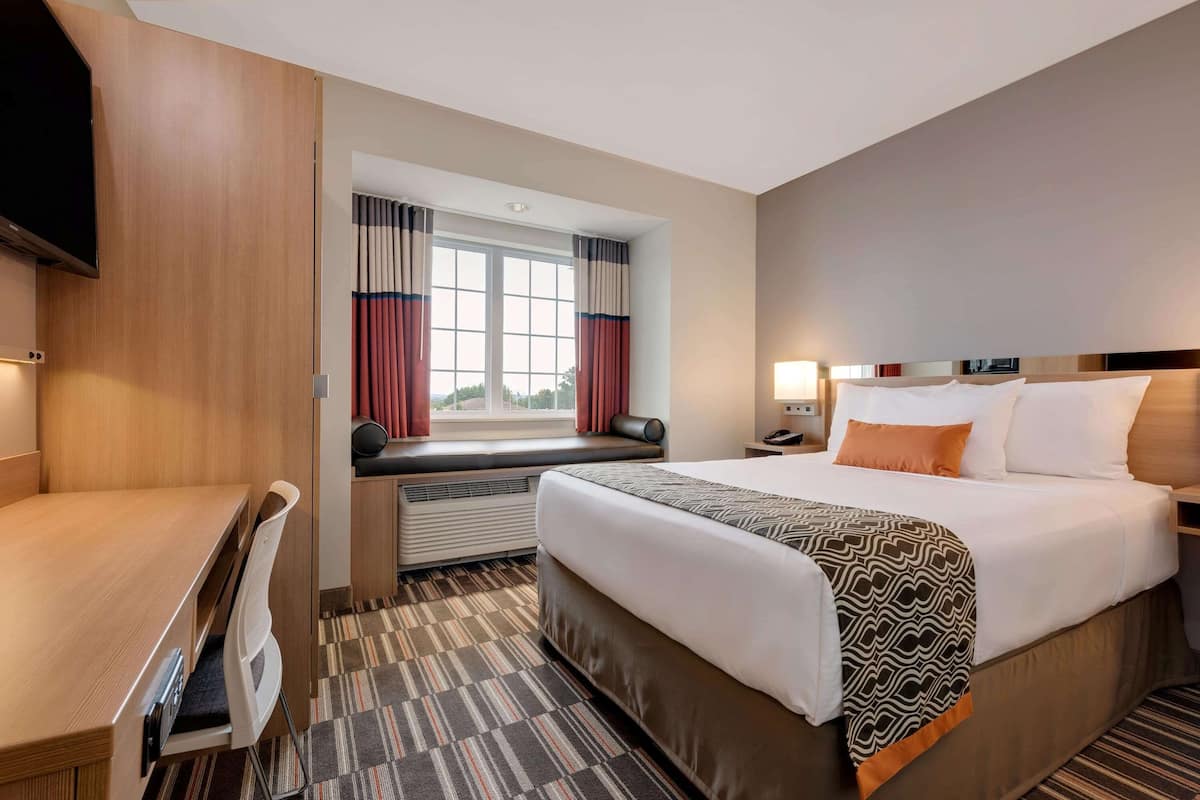 Habitación de hotel con cama, escritorio, televisión, ventana con cortinas y vistas al exterior.