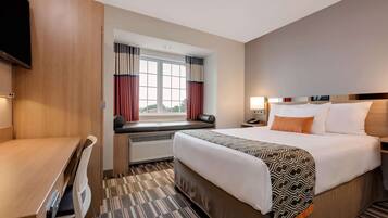 Habitación de hotel con cama, escritorio, televisión, ventana con cortinas y vistas al exterior.