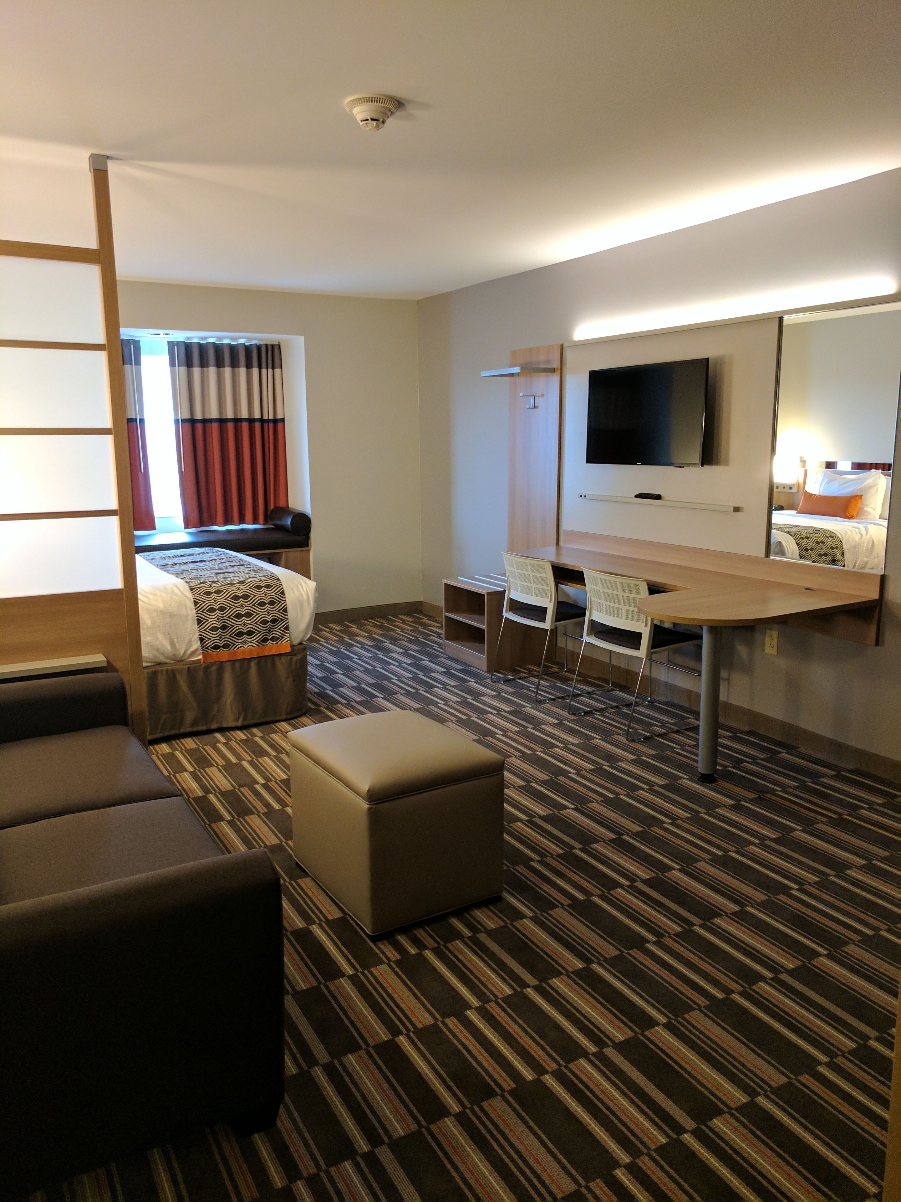 A hotel room with a bed, a desk, a chair, a television, and a large mirror.