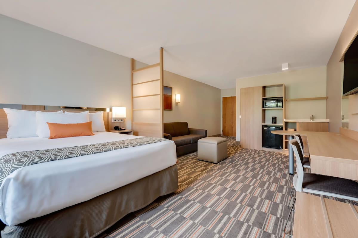 Habitación de hotel con una cama grande, un sofá, una mesita, un televisor y una zona de kitchenette.