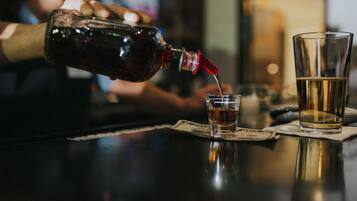 A person pouring a dark liquid from a bottle into a glass on a bar counter.