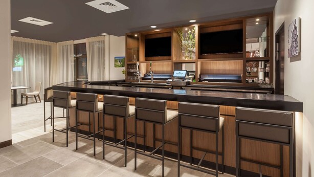 Una cocina moderna con una isla central, taburetes de bar, iluminación empotrada y un televisor integrado.