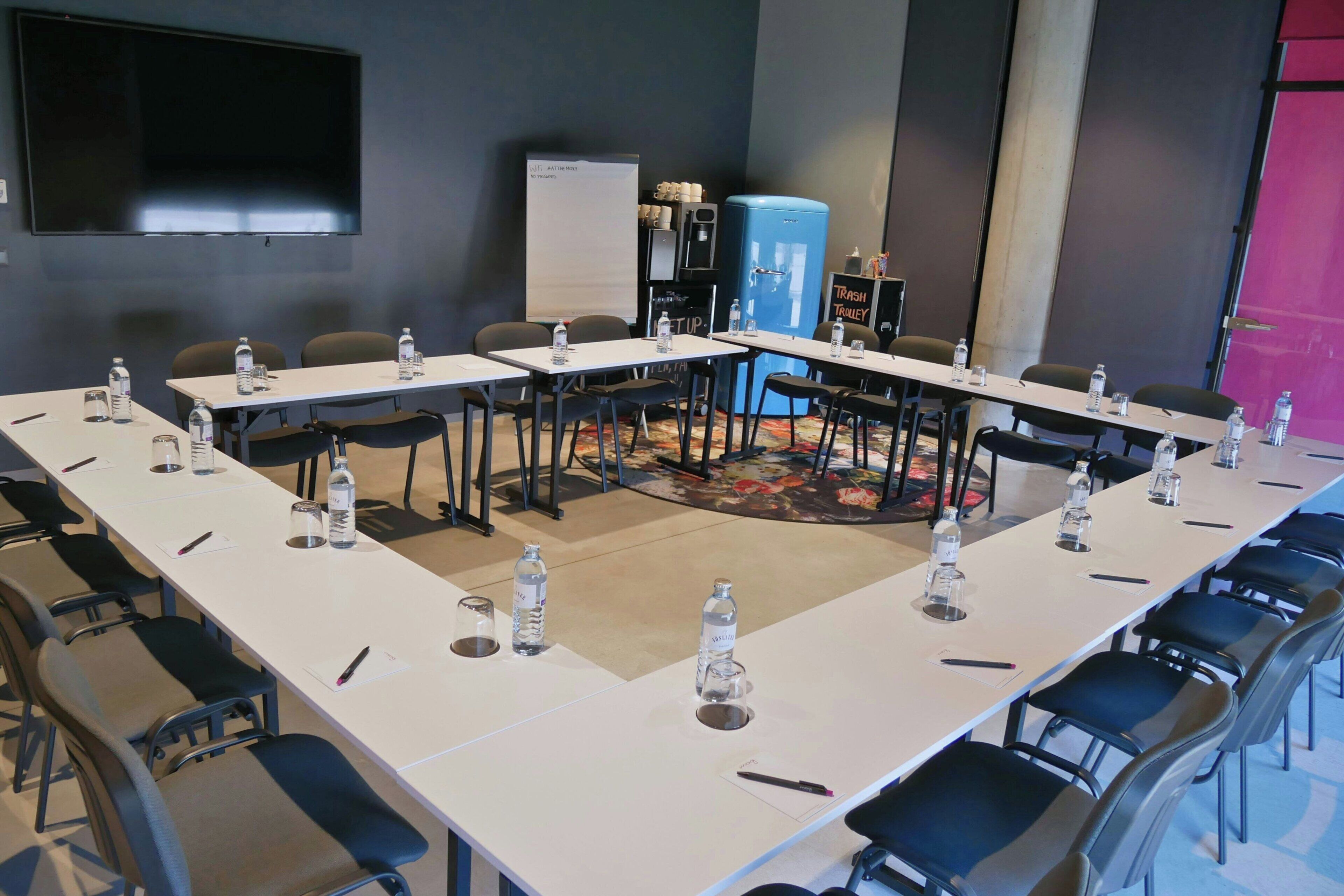 Ein Konferenzraum mit langen Tischen, Stühlen, Wasserflaschen und einer Whiteboard-Tafel.