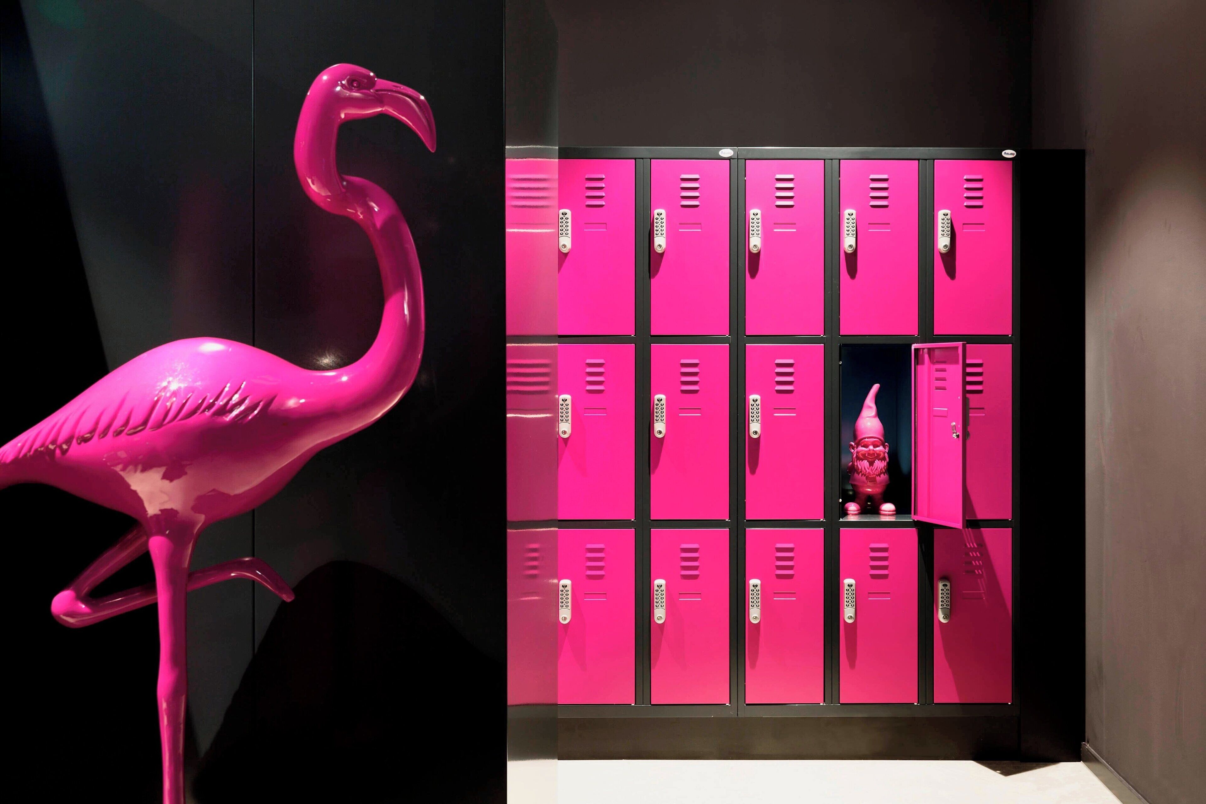 Eine rosa Flamingo-Skulptur neben einer Reihe pinkfarbener Schließfächer, in einem davon befindet sich eine kleine Statue.