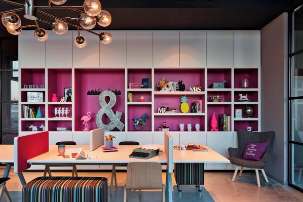 A modern workspace with a white desk, a red partition, and a bookshelf filled with books and decorative items. - Moxy Vienna Airport (Schwechat)