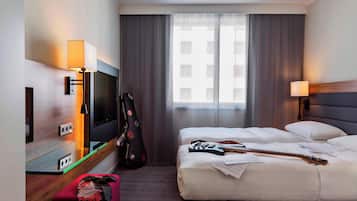 Una habitación de hotel con una cama, un televisor, una guitarra y una maleta.
