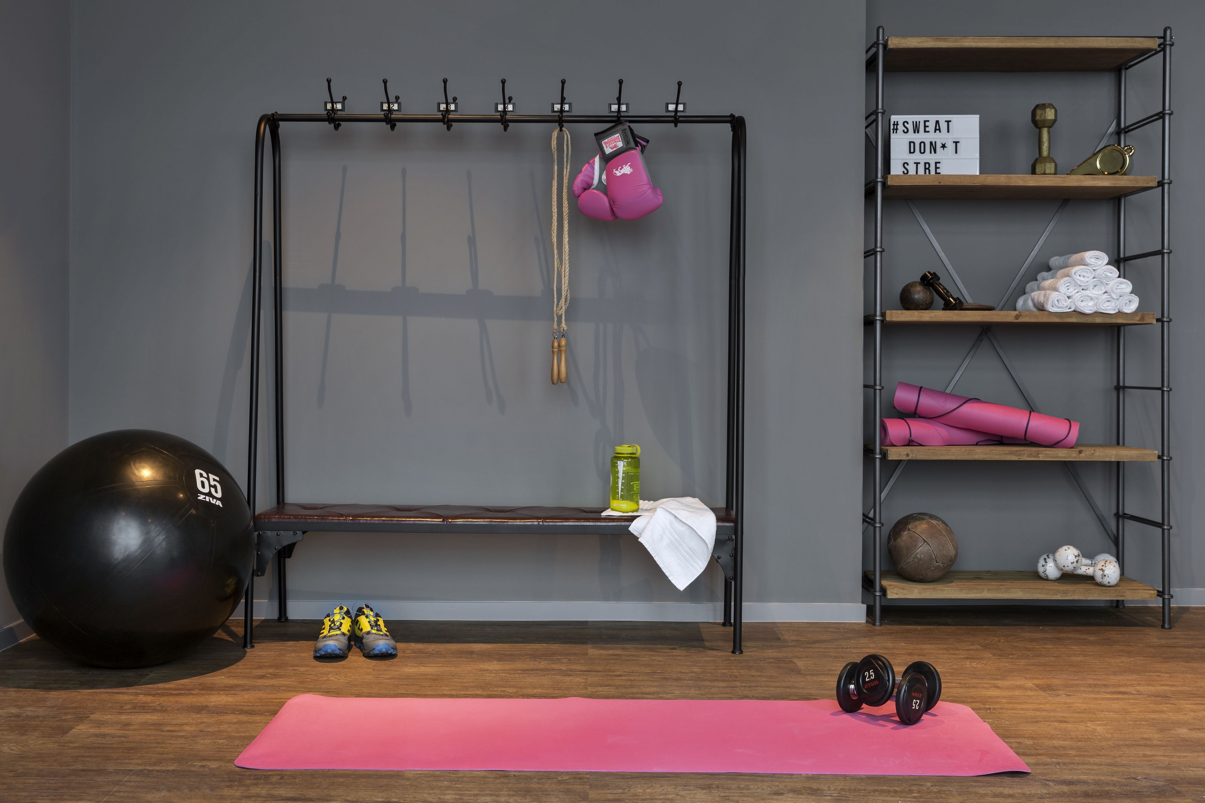 Uma academia com barra de exercícios, bola de ginástica, halteres, tapete de yoga e prateleiras com equipamentos de fitness.