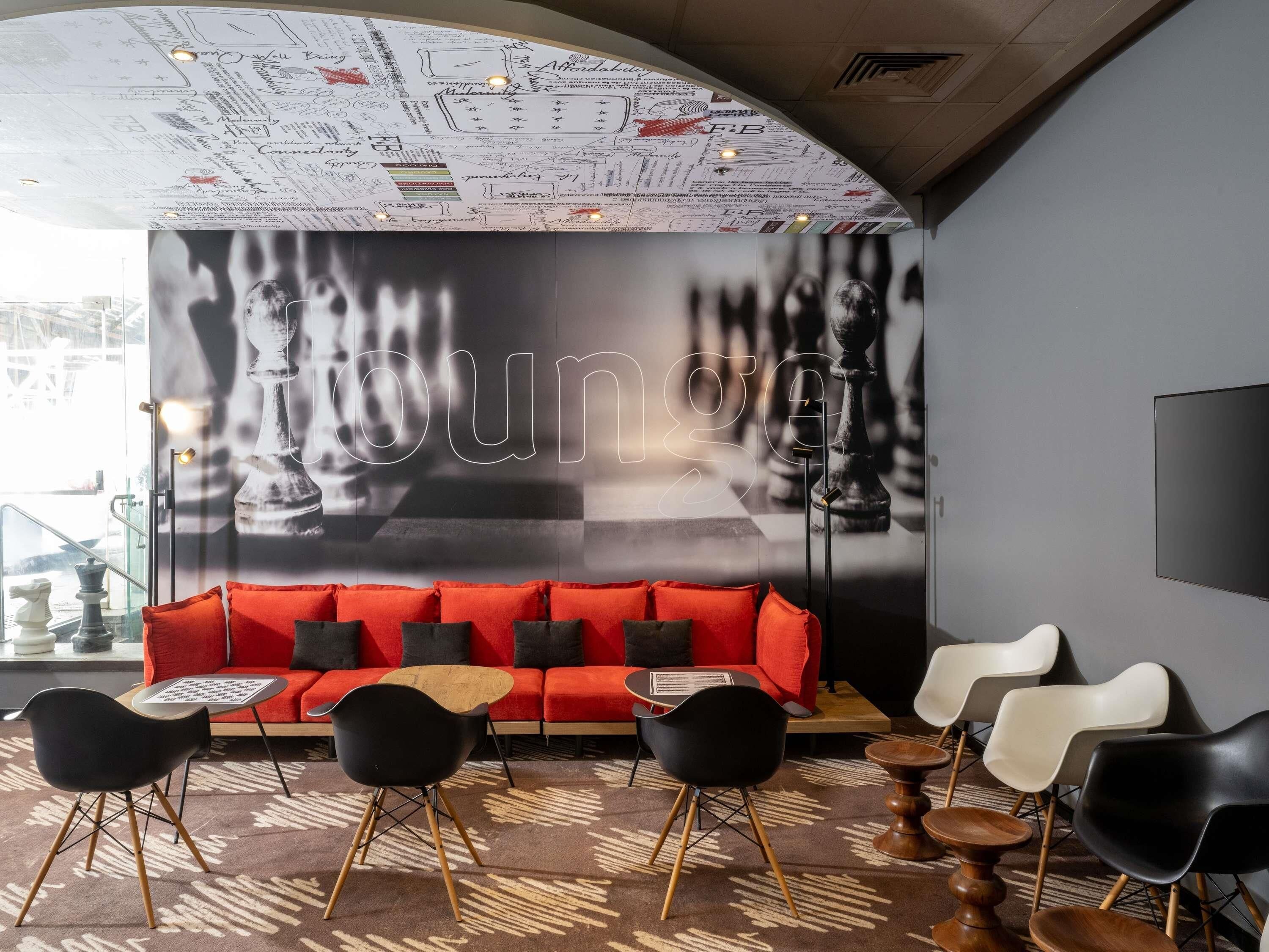 A lounge area with a red sofa, black and white chairs, and a chessboard design on the wall.
