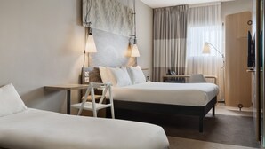 A hotel room with two beds, a desk, a chair, a TV, and a large window with curtains.