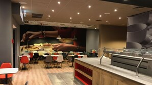 A restaurant with a modern interior, featuring a counter with a glass display, multiple tables and chairs, and a wall with a large image of hands preparing food. - ibis Jerusalem city Center -  An AccorHotels Brand (Jerusalem)