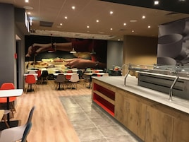 Un restaurante con una decoración moderna, que cuenta con una barra con vitrina, varias mesas y sillas, y una pared con una imagen grande de manos preparando comida.