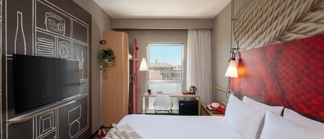 A hotel room with a bed, a desk, a TV, and a view of the city.
