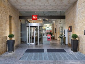 Entrada de hotel con puerta giratoria, fachada de vidrio y cartel que dice 'Ibis Jerusaam City Center Hotel'.