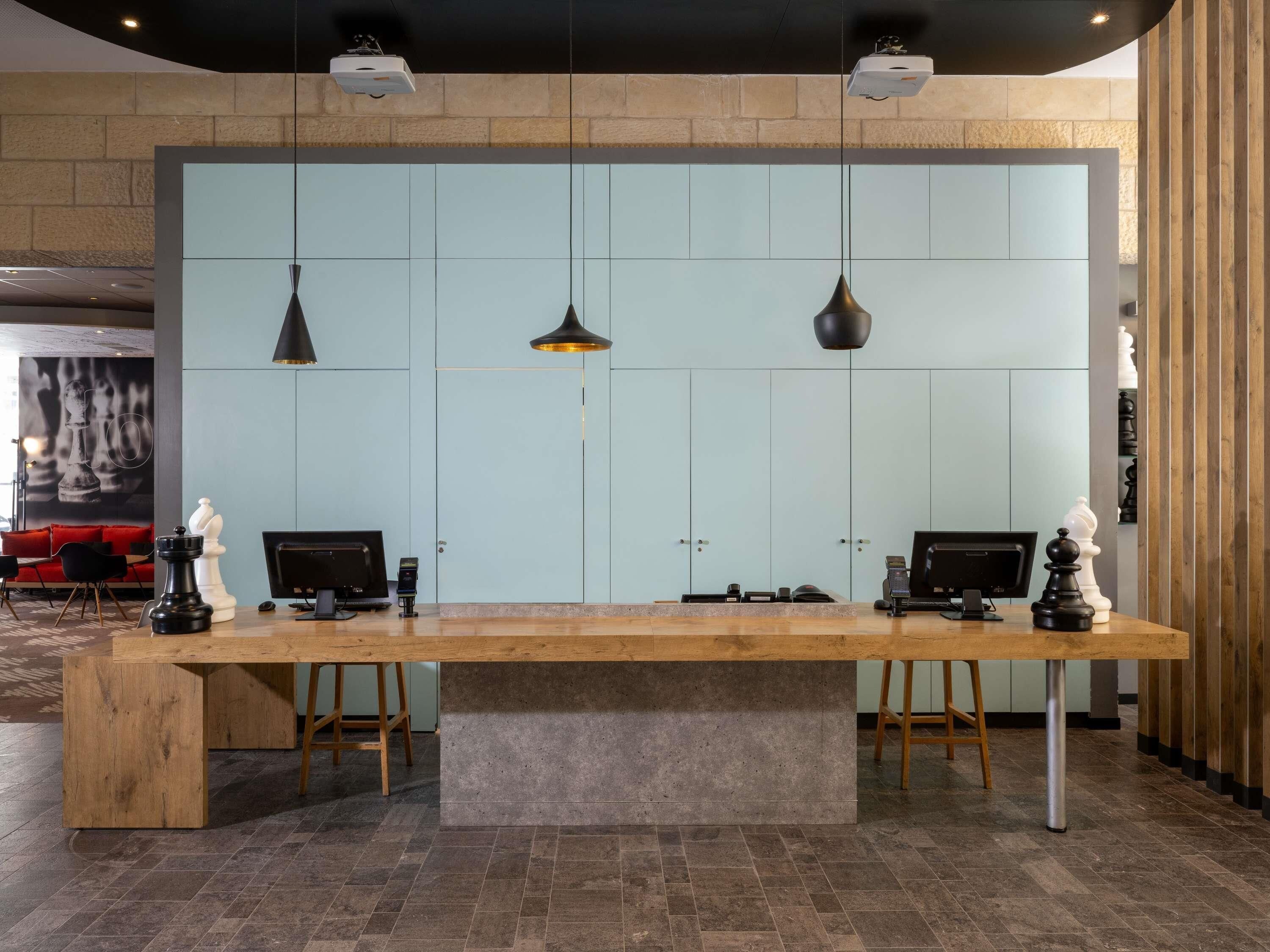 A reception desk with two computer monitors, a wooden table, and a light blue wall with a chessboard design.