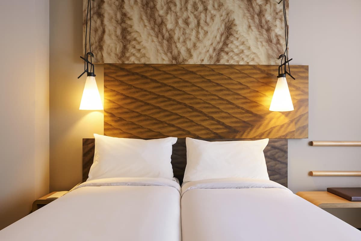 Una cama doble con dos almohadas, un cabecero de madera con diseño en espiga y dos lámparas colgantes.