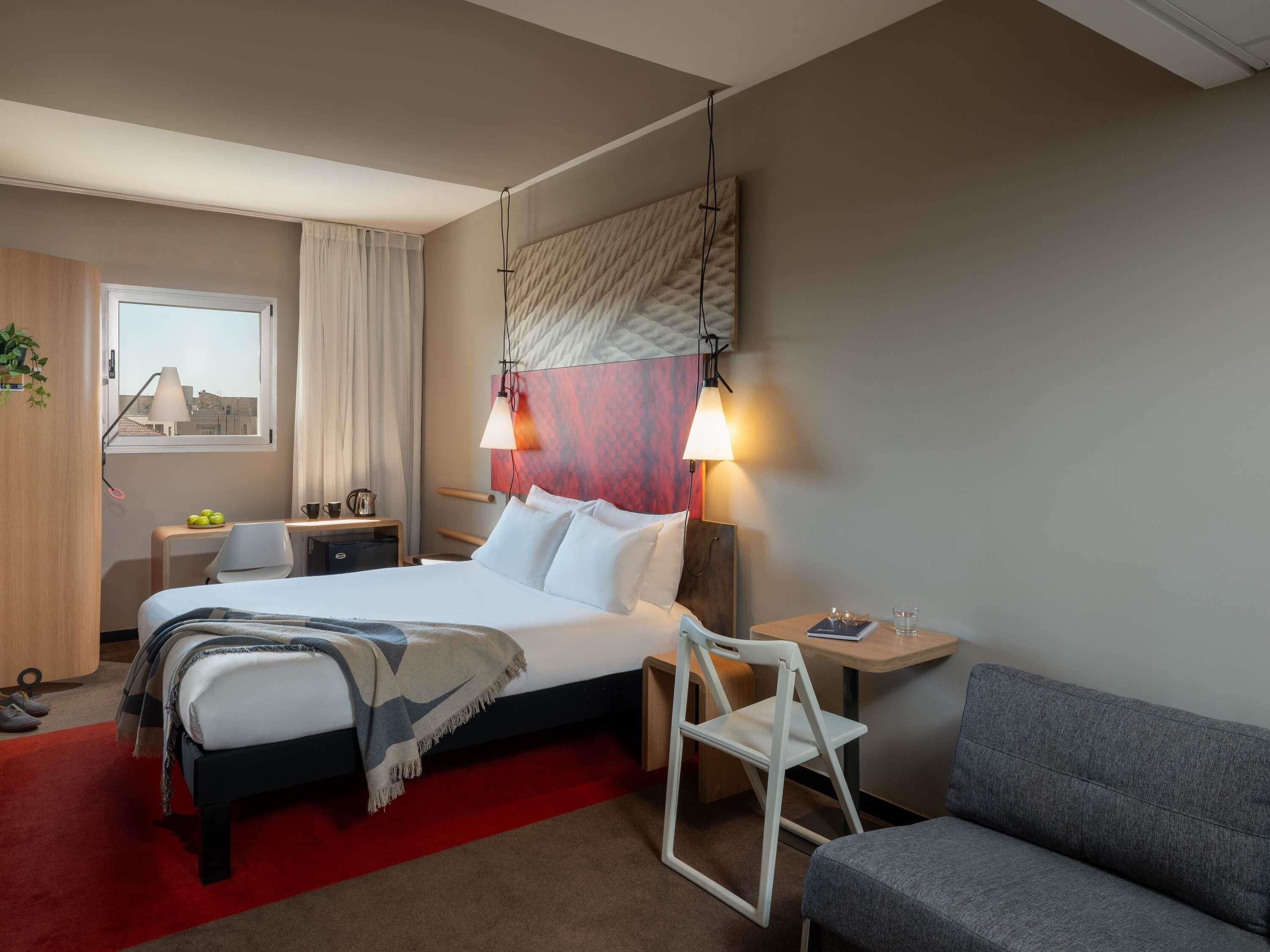 A hotel room with a bed, bedside table, chair, and a sofa.