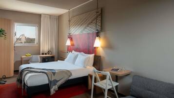 A hotel room with a bed, bedside table, chair, and a sofa.