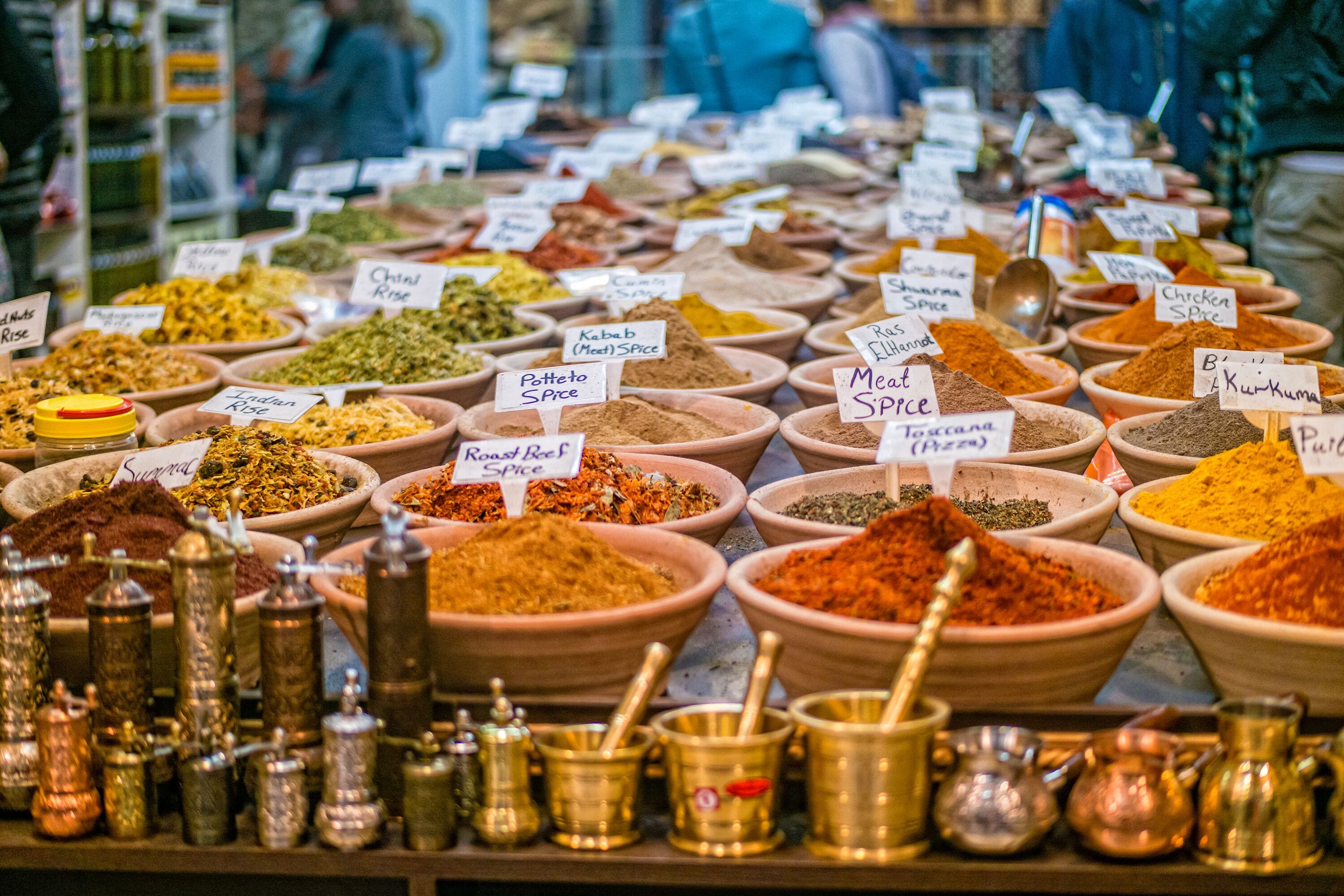 A market stall with various spices and condiments in bowls, each labeled with their names.