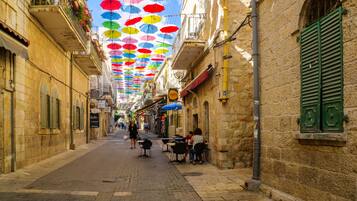 Una calle estrecha con edificios de piedra, mesas al aire libre y sombrillas de colores.