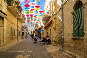 A narrow street with stone buildings, outdoor seating, and colorful umbrellas.