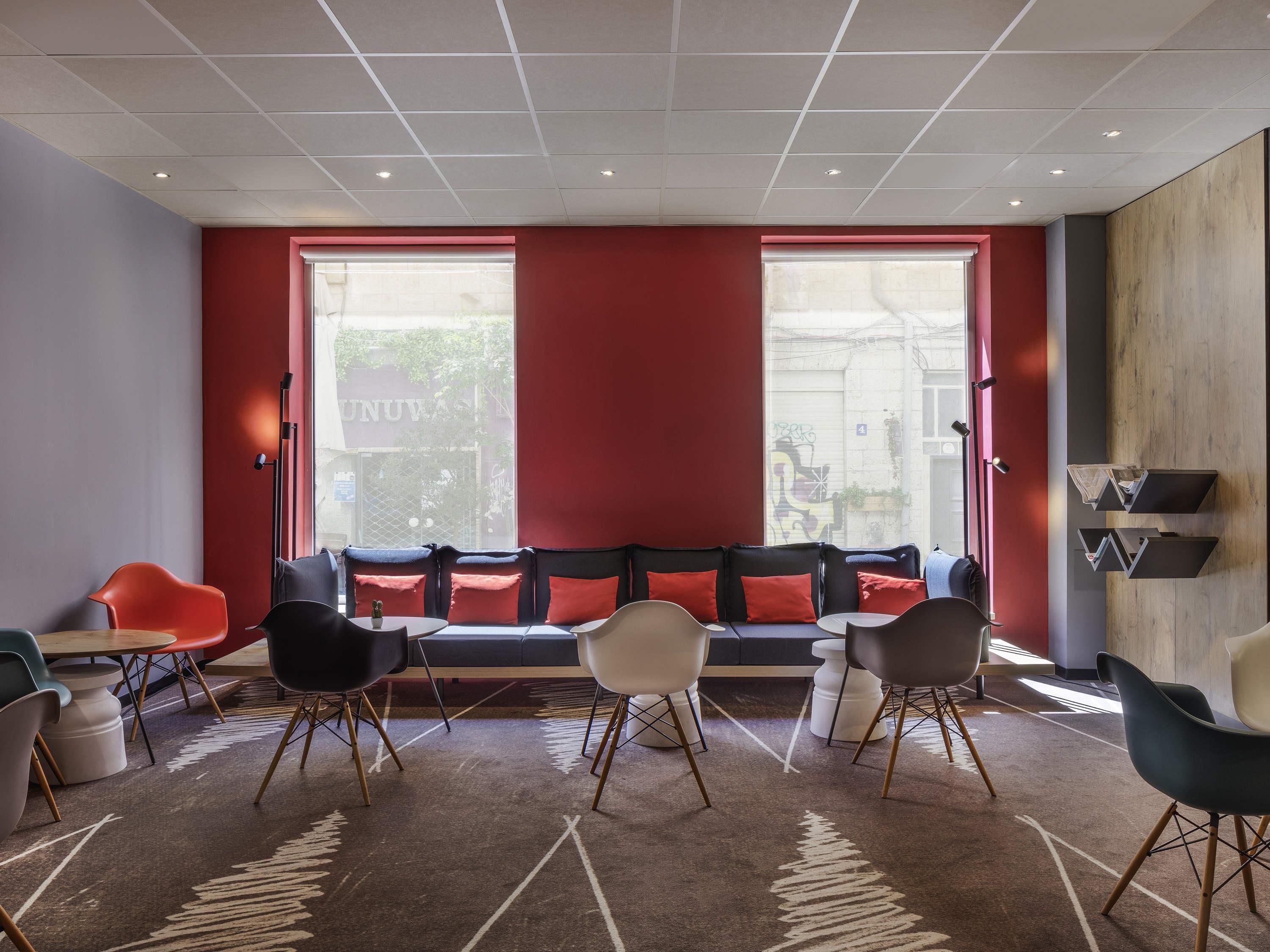 A modern interior with a red accent wall, a seating area with multiple chairs and a sofa, and a view through large windows.