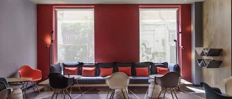 A modern interior with a red accent wall, a seating area with multiple chairs and a sofa, and a view through large windows.