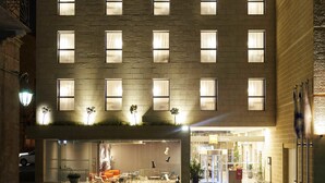 Un hotel con fachada moderna, múltiples ventanas y acceso directo al nivel de la calle con asientos exteriores.