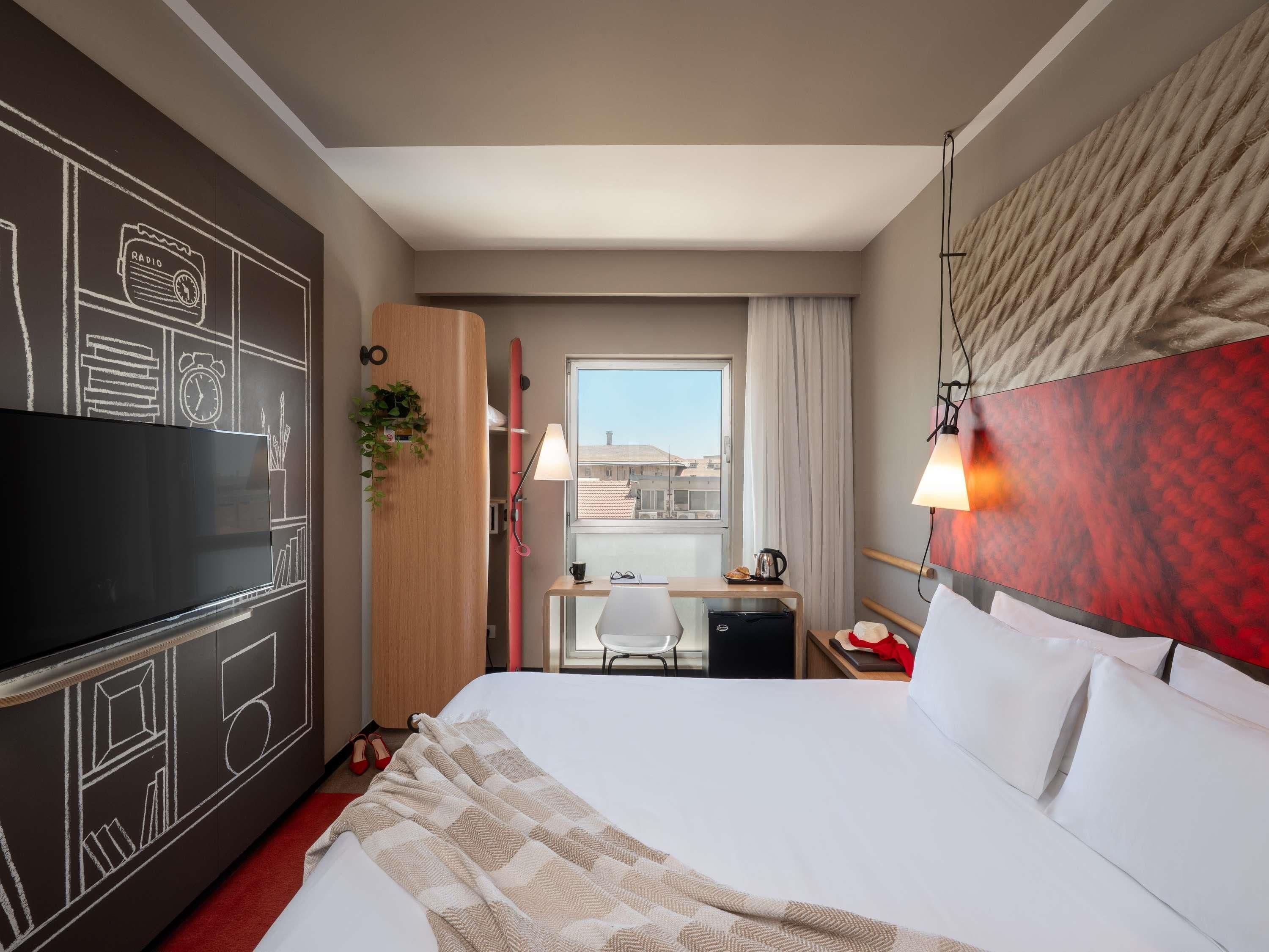 A hotel room with a bed, a desk, a TV, and a window with a view.