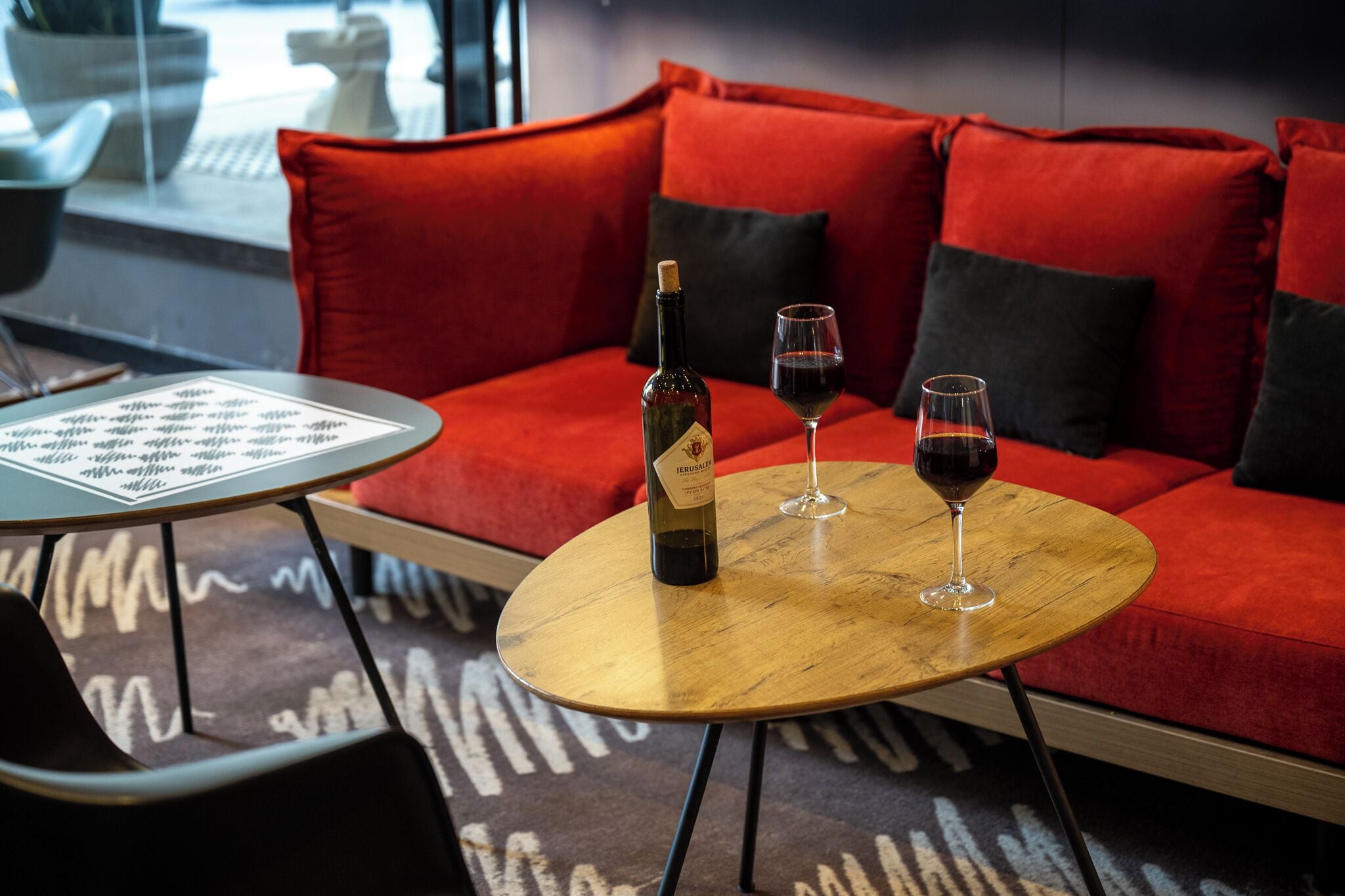 Un rincón acogedor con un sofá rojo, una mesa de madera y dos copas de vino tinto.