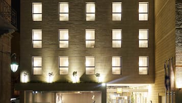 Un hôtel doté d’une façade moderne, de nombreuses fenêtres et d’une entrée au niveau du sol avec un espace extérieur aménagé pour s’asseoir.