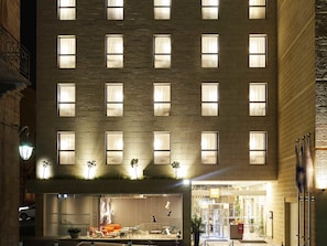 Un hotel con fachada moderna, múltiples ventanas y acceso directo al nivel de la calle con asientos exteriores.