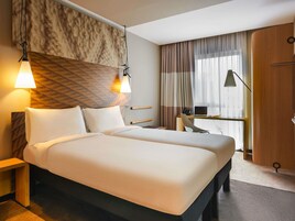 Habitación de hotel con una cama grande, mesitas de noche, un escritorio con una computadora portátil y una ventana con cortinas.