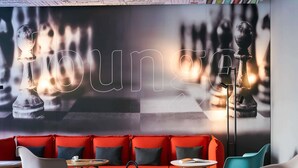 Un área de descanso con un sofá rojo, un mural de un tablero de ajedrez y sillas modernas.
