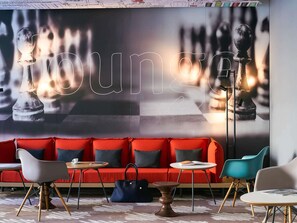 Un área de descanso con un sofá rojo, un mural de un tablero de ajedrez y sillas modernas.