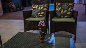 Two wicker chairs with floral cushions, a small potted orchid on a table, and a tiled floor. - Adelante Lodge (Bloemfontein)