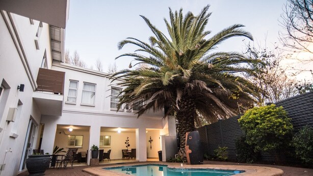 A residential pool area with a palm tree, a dining table, and chairs. - Adelante Lodge (Bloemfontein)