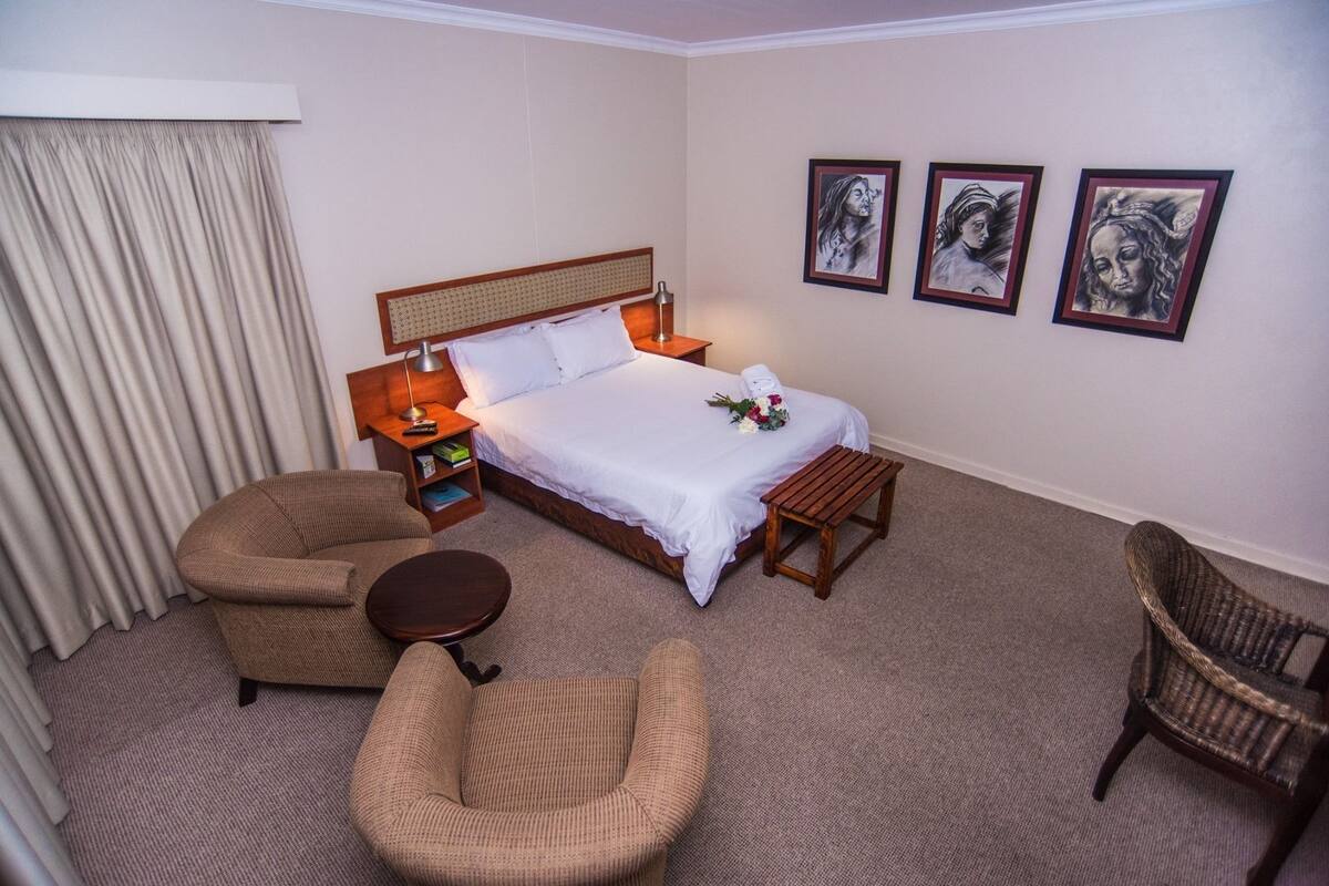 Une chambre d’hôtel avec un lit, deux chaises, une petite table et des œuvres d’art accrochées au mur.